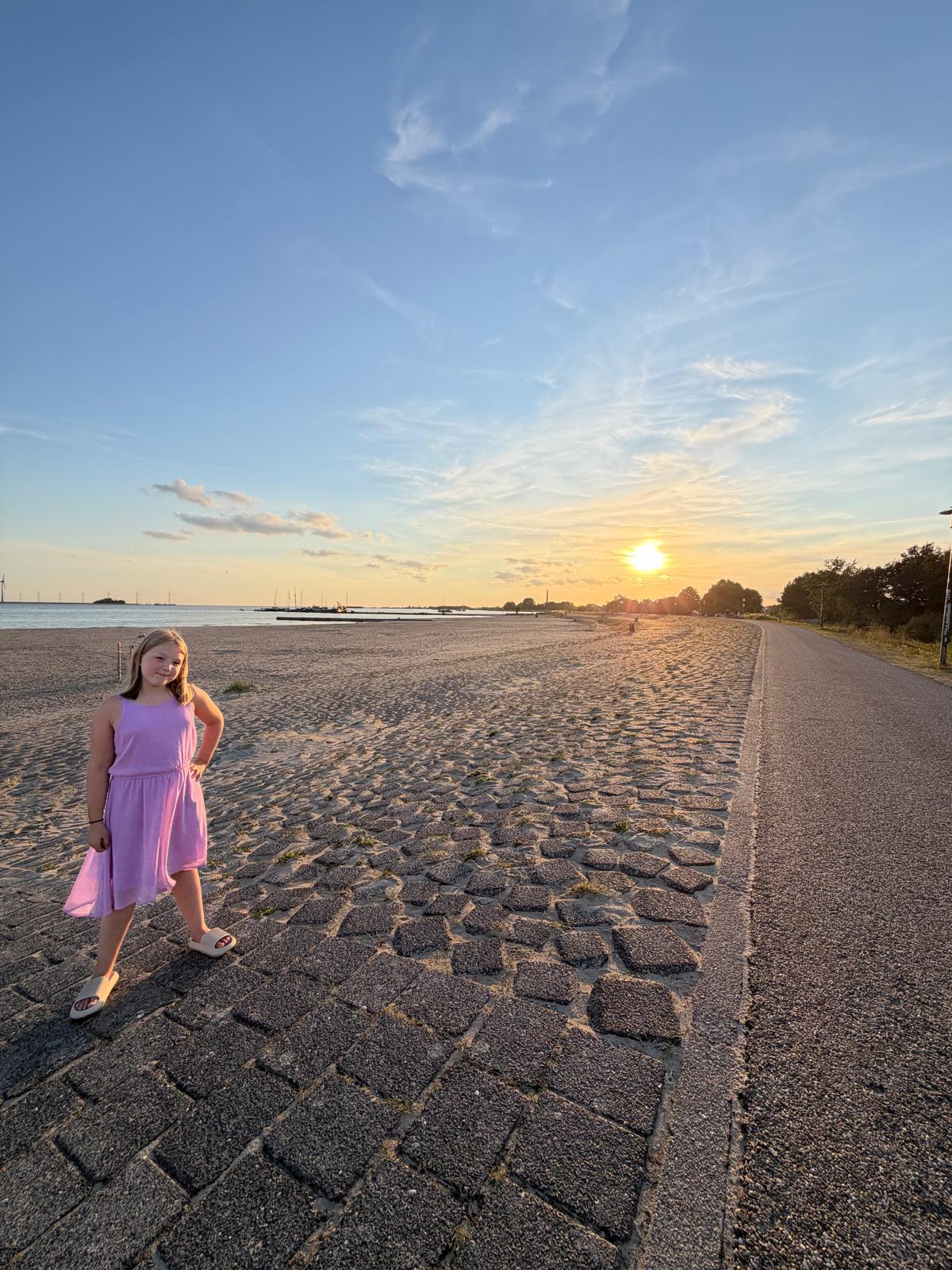 Daisy in een roze jurk op het strand bij zonsondergang